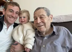 Kevin, his young child and Opa smiling together on Opa’s sofa